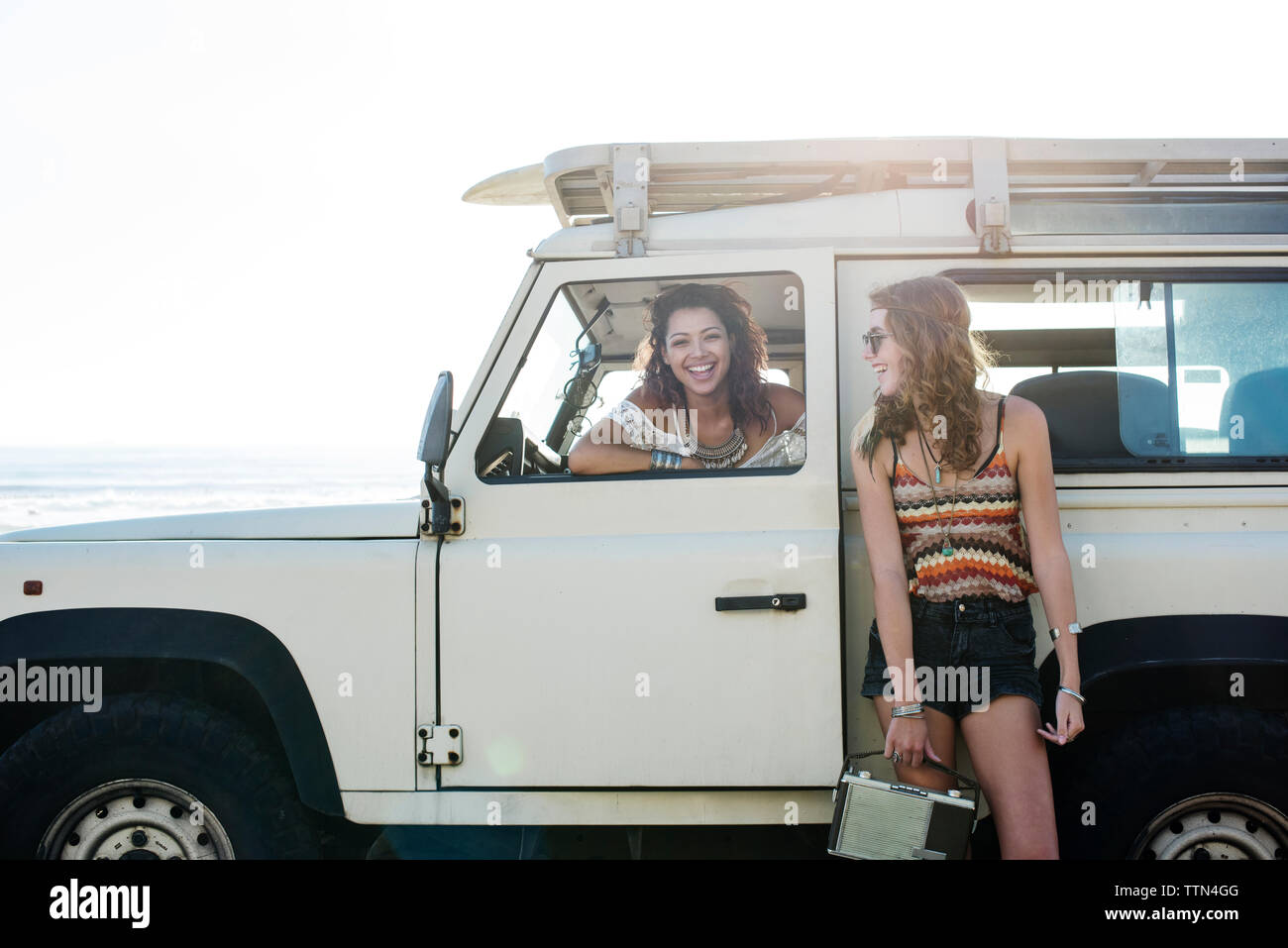Happy woman looking at friend sitting in off-road vehicle during sunny day Stock Photo