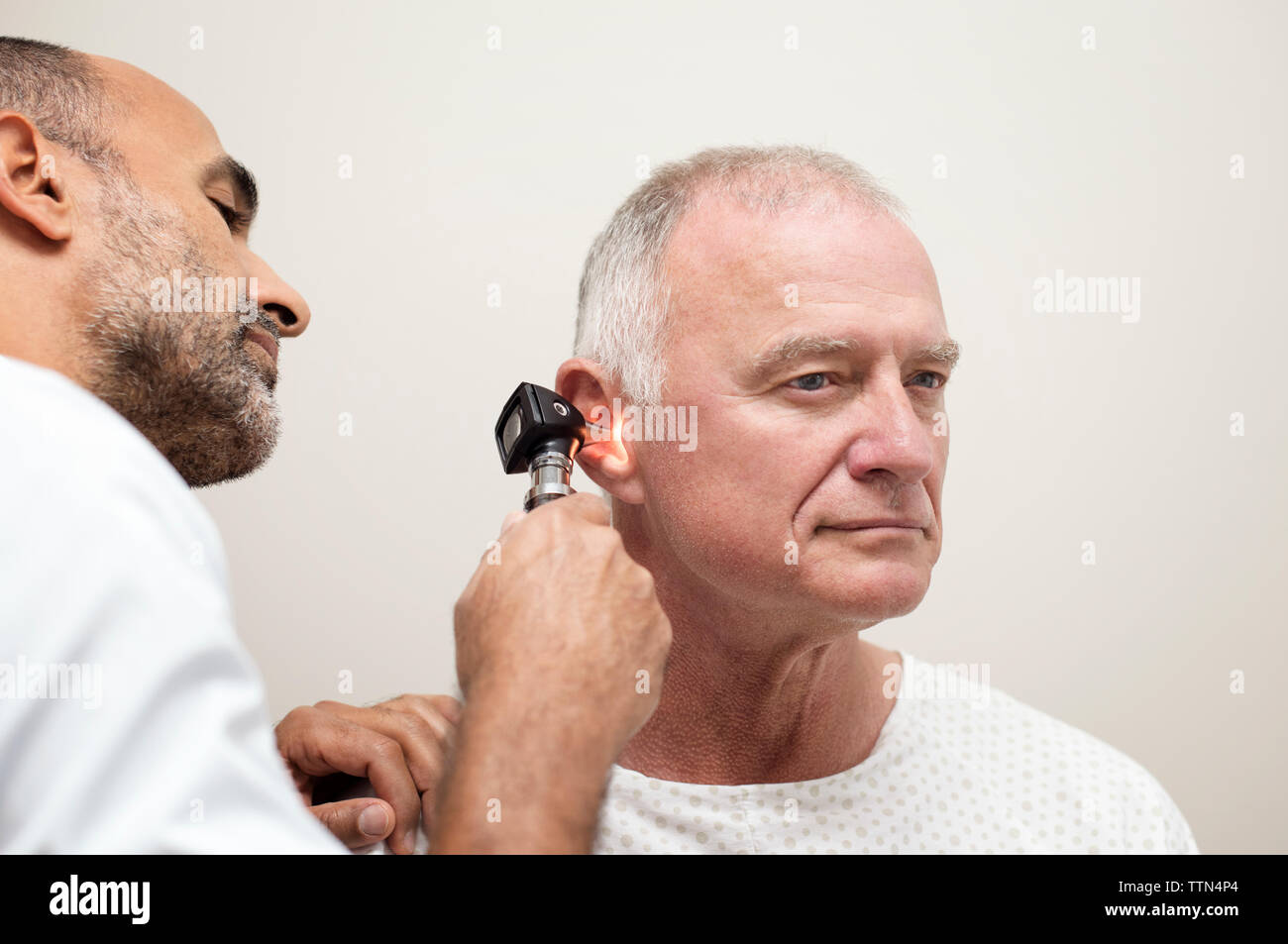 Doctor using otoscope while examining patient's ear in hospital Stock