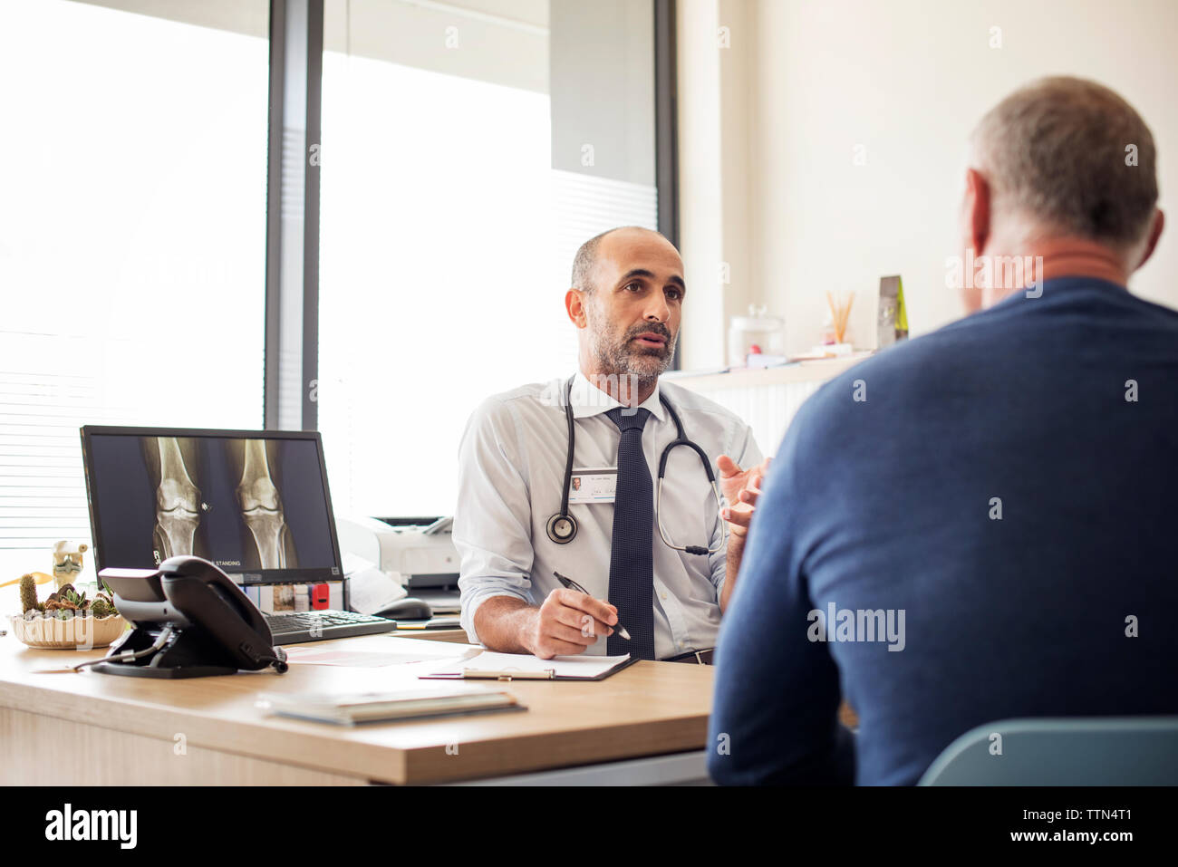 Doctor discussing with patient while sitting at desk in hospital Stock ...