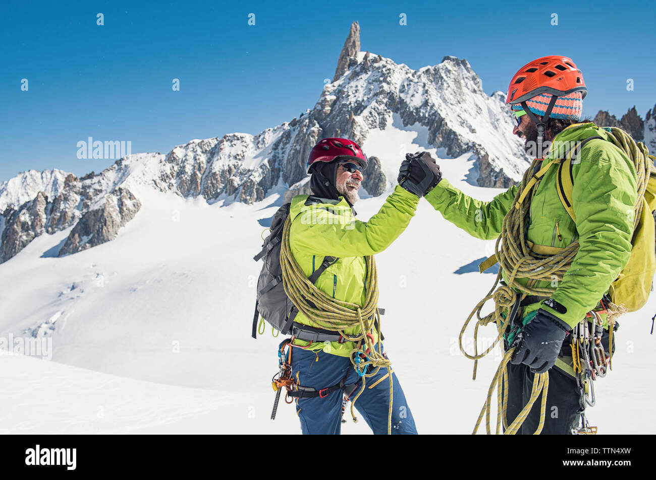 Happy hikers giving high-five while standing on snow covered mountain against clear blue sky Stock Photo