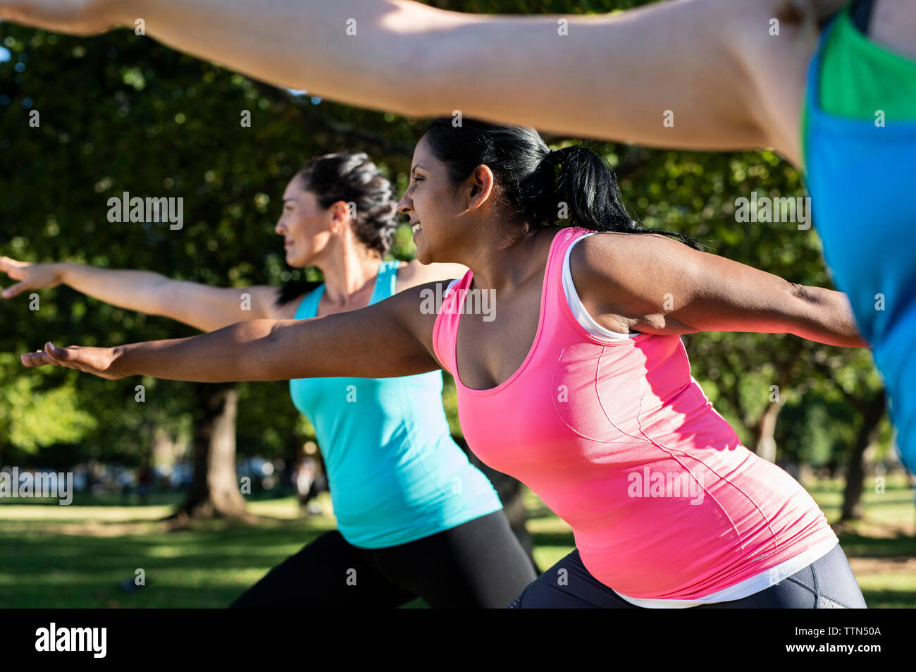 Low angle view of friends with arms outstretched exercising against trees in park Stock Photo