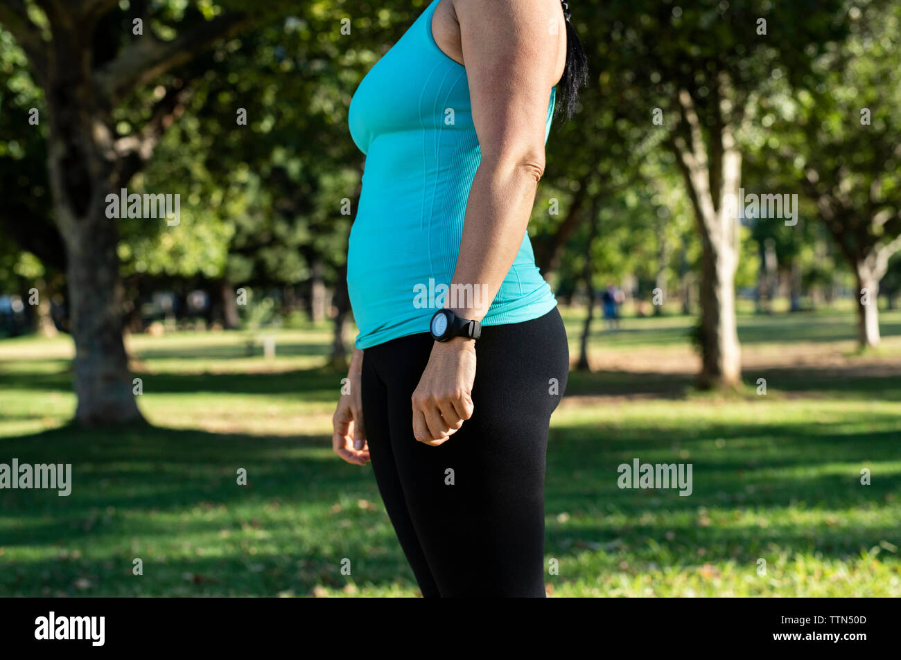 Midsection of woman in sports clothing standing against trees at park Stock Photo
