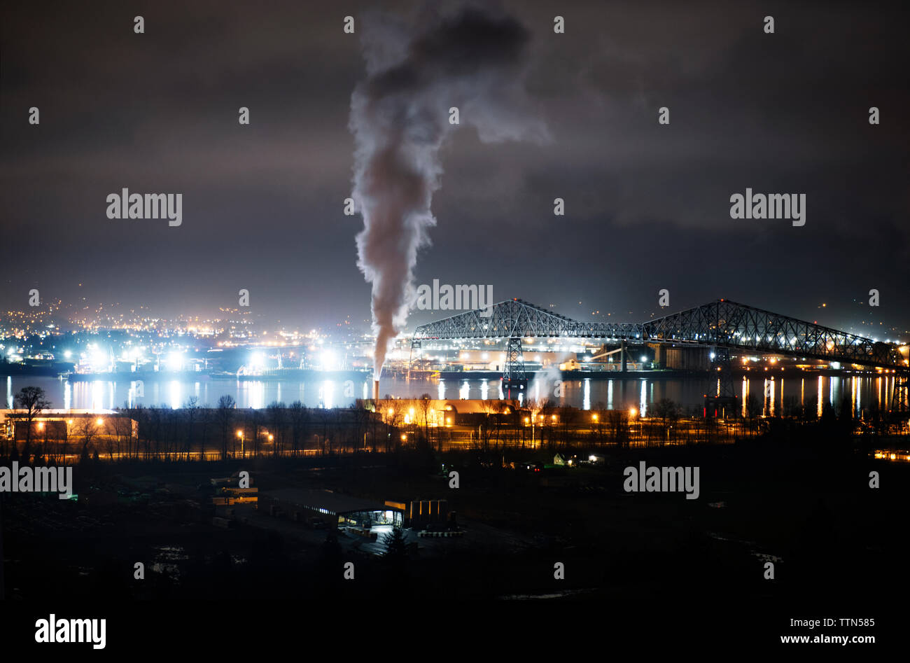 Smoke emitting from chimney at factory in illuminated city at night Stock Photo