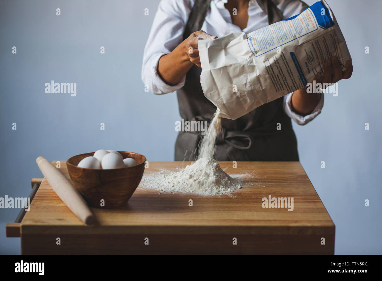 Midsection of woman removing flour from packet on table against wall Stock Photo