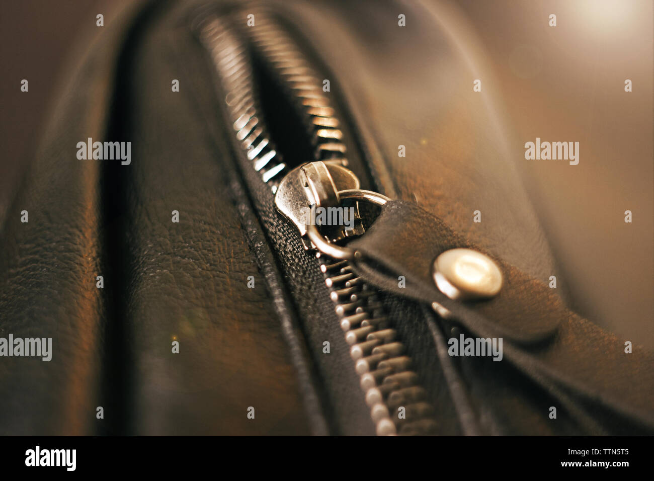 Metal zipper on the pocket on the black leather bag, illuminated by light Stock Photo