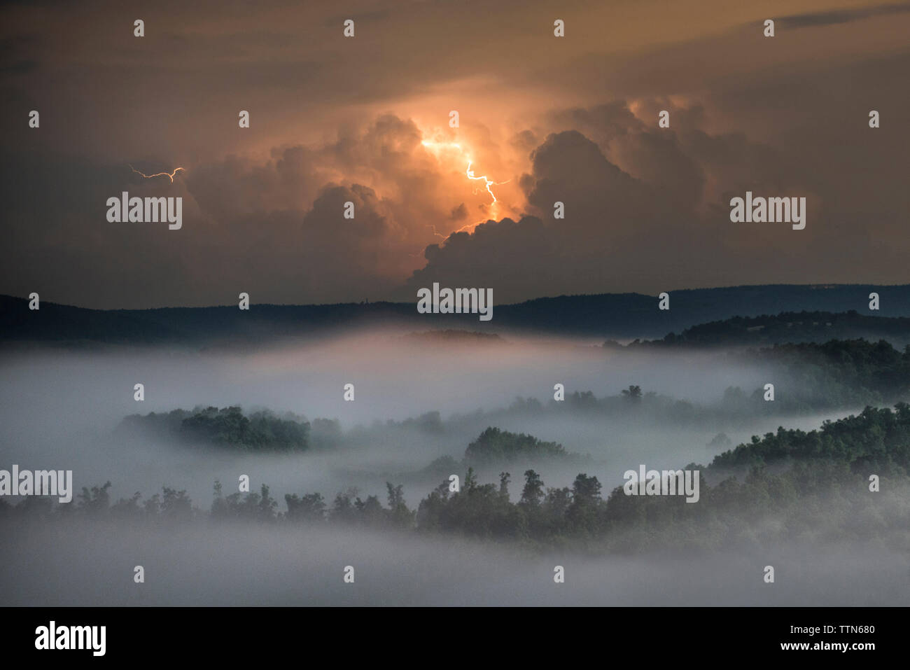 Lightning clouds over forest and mountain at night Stock Photo