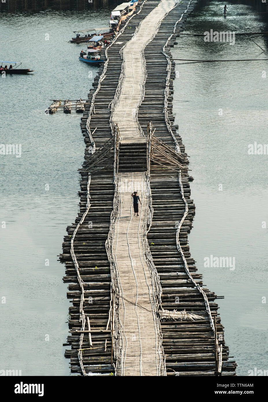 Distant view of man walking on footbridge amidst river Stock Photo