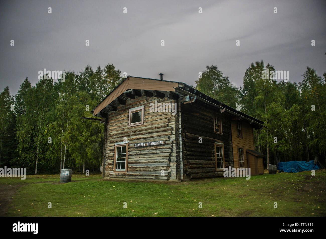 Slaven's roadhouse on field by trees at Yukon Charley Rivers National Preserve against cloudy sky Stock Photo