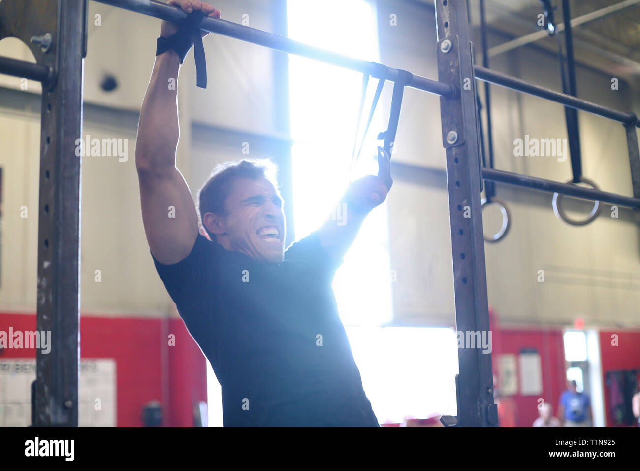 Aggressive male adaptive athlete screaming while doing chin-ups in gym Stock Photo