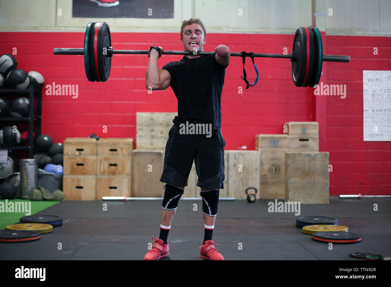 Confident male adaptive athlete lifting barbell while standing against ...
