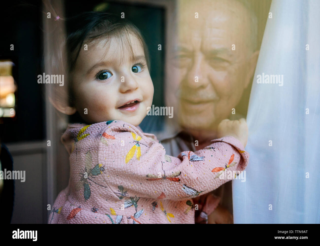 Portrait of cute granddaughter carried by grandfather seen through window Stock Photo