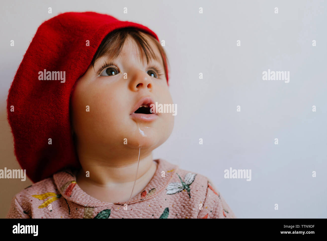 Close-up of cute baby girl drooling while looking up against wall at home Stock Photo