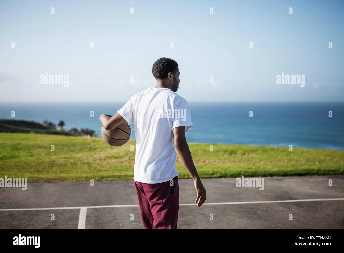 Man with basketball at court by sea against sky Stock Photo