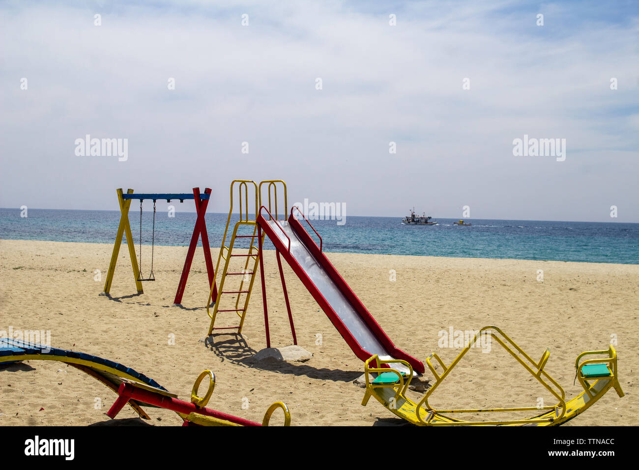 Childrens Playground situated on the beach at Nea Skioni,Halkidiki , Greece with a fishing trawler in the background. Stock Photo