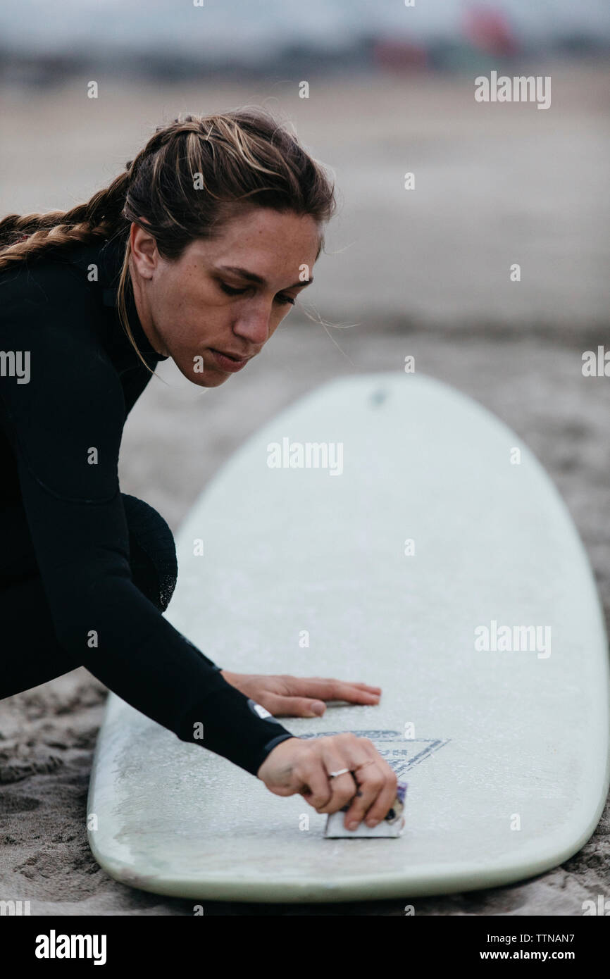 Side view of woman polishing surfboard while crouching on sand at beach