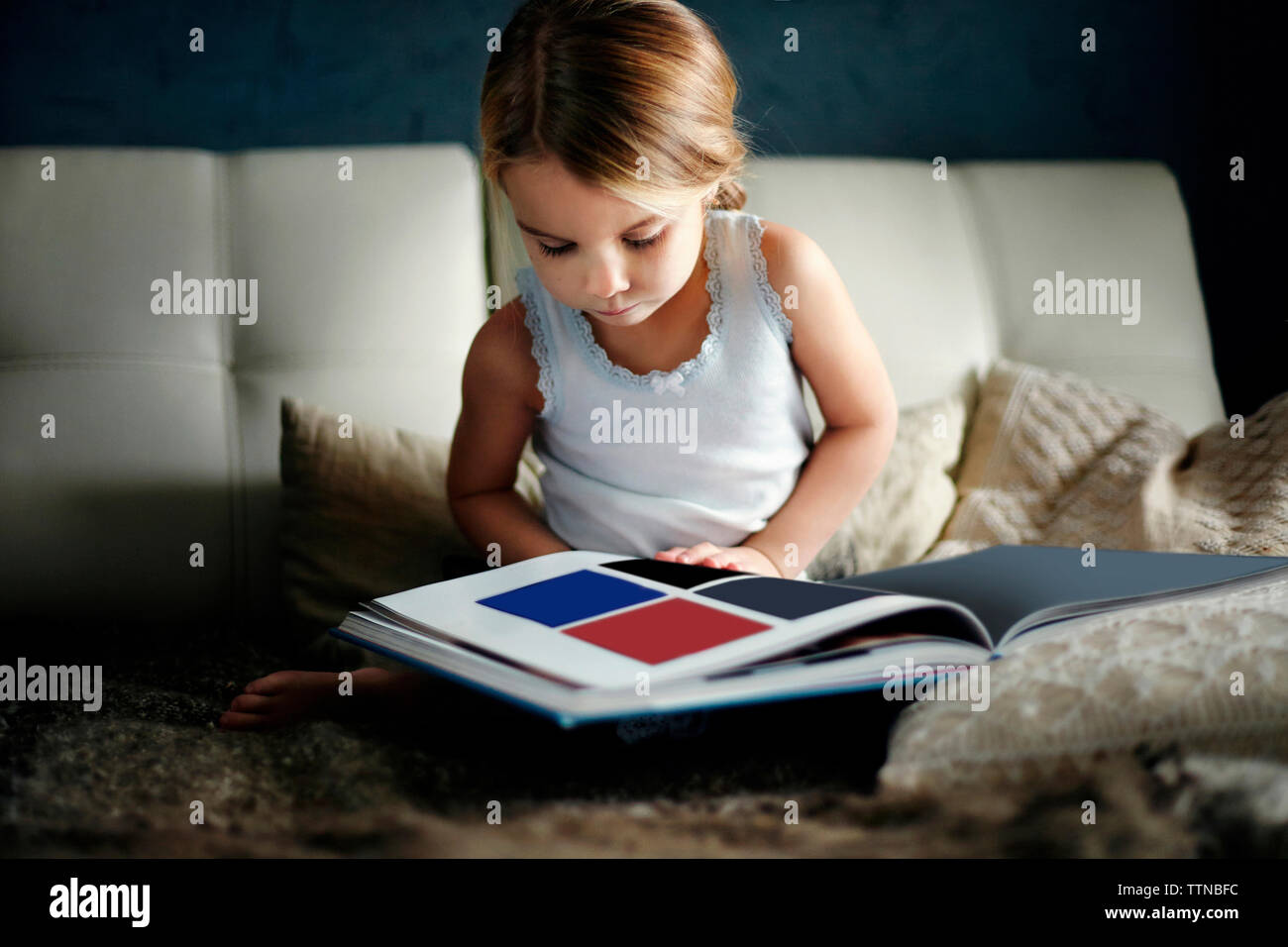 Girl looking at book while sitting on bed Stock Photo - Alamy