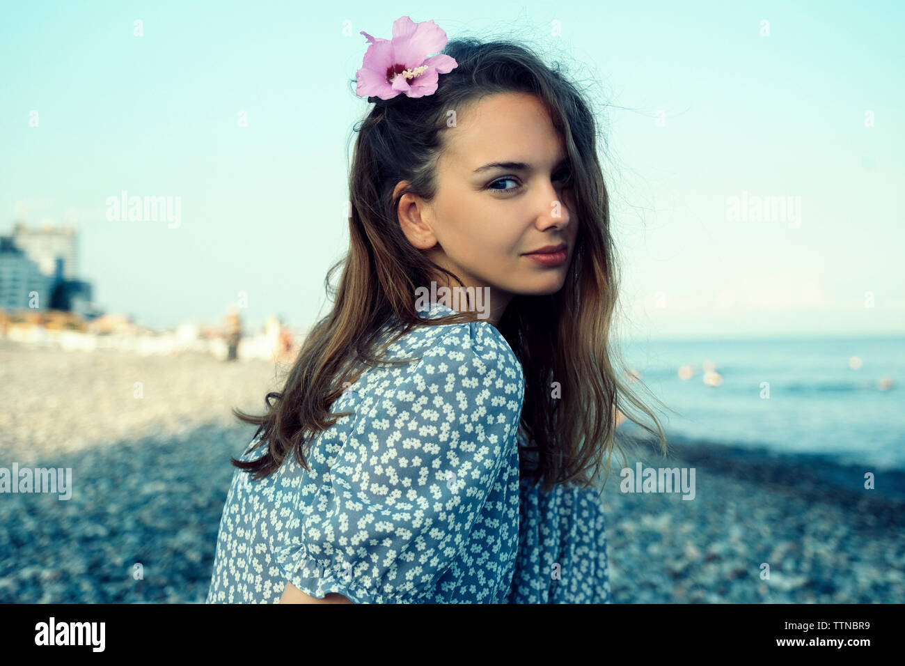 Portrait of woman wearing flower while sitting at beach against clear sky Stock Photo