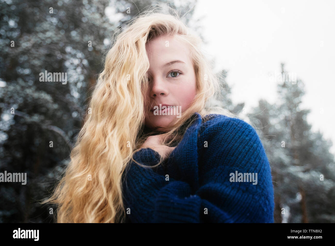 Low angle portrait of woman with blond hair standing against trees in ...