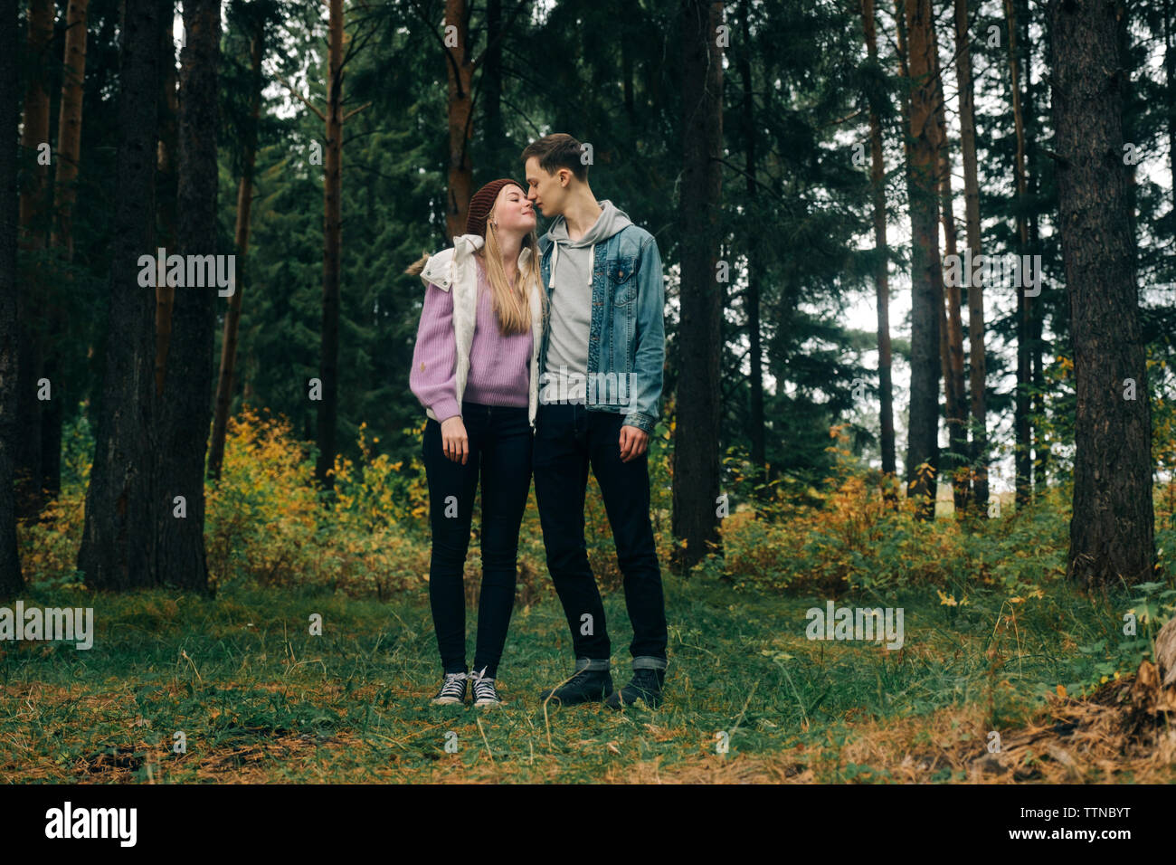 Romantic young couple standing on grassy field against trees in forest Stock Photo