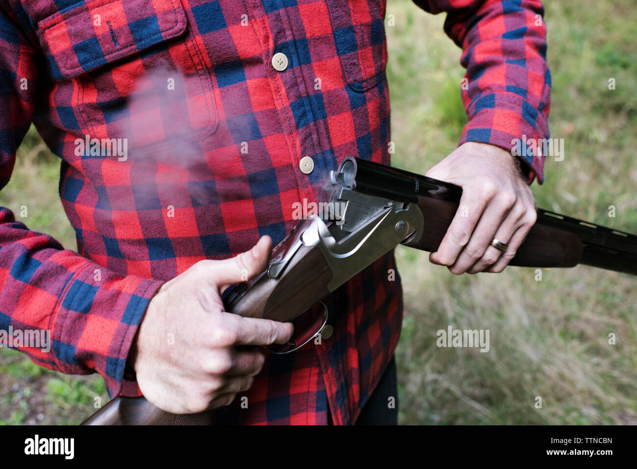 Midsection of man unloading shotgun while standing on field Stock Photo