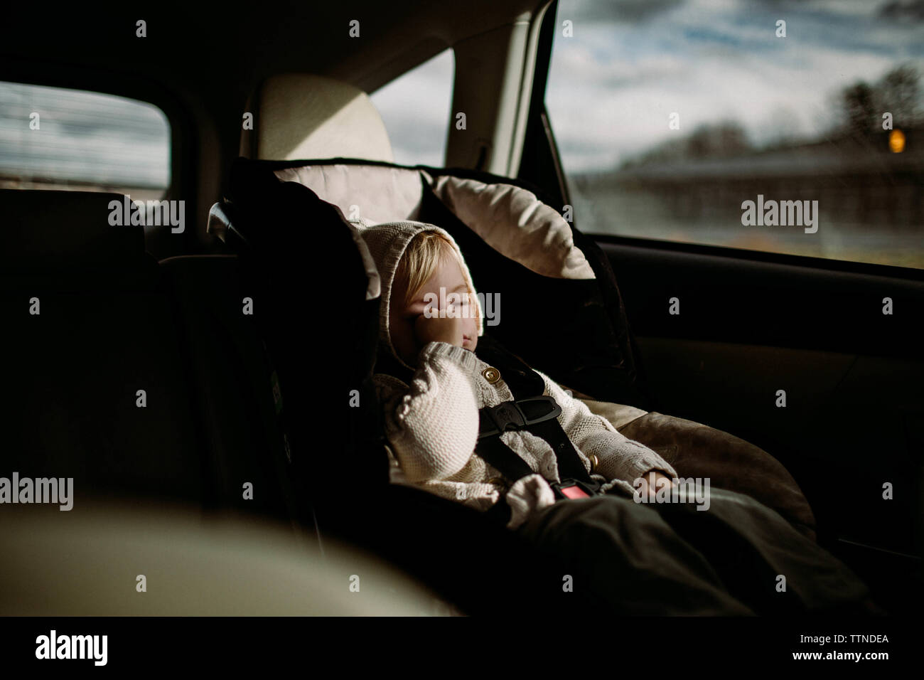 Toddler rubbing her eye, asleep in carseat, driving through city Stock Photo