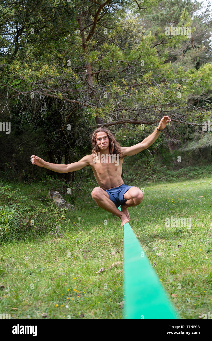 Active young man with naked torso balancing on slackline in green field on summertime Stock Photo