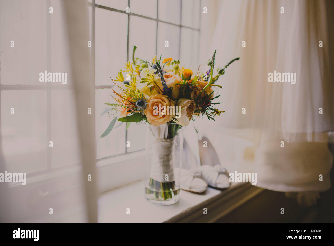 Flower vase and shoes on window sill by wedding dress Stock Photo