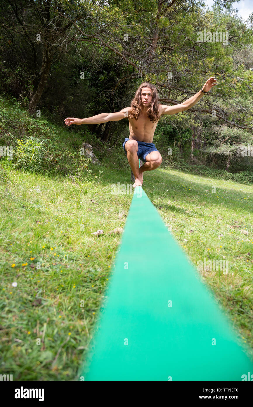Active young man with naked torso balancing on slackline in green field on summertime Stock Photo