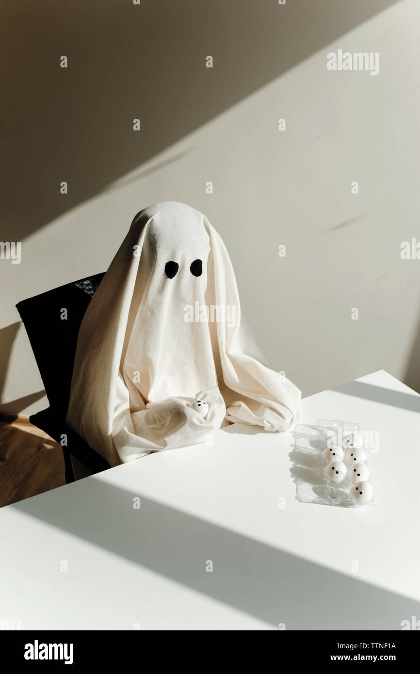 High angle view of man in ghost costume with egg carton on table sitting at home during Halloween Stock Photo