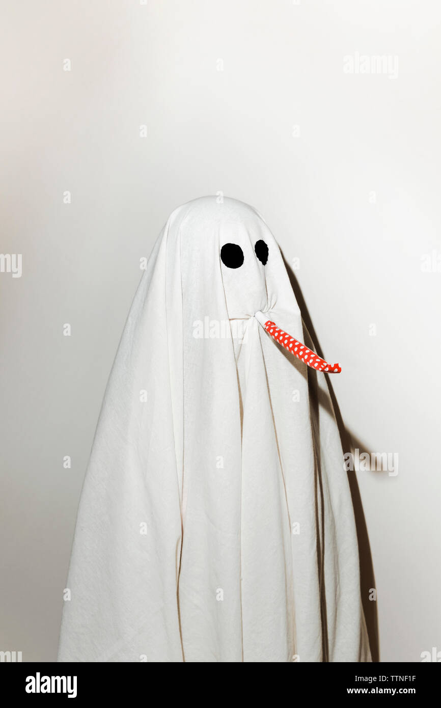 Man in ghost costume blowing party horn blower while standing against