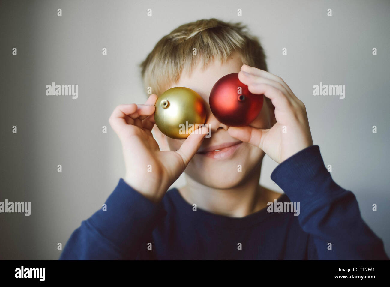 Playful boy holding baubles against face at home Stock Photo