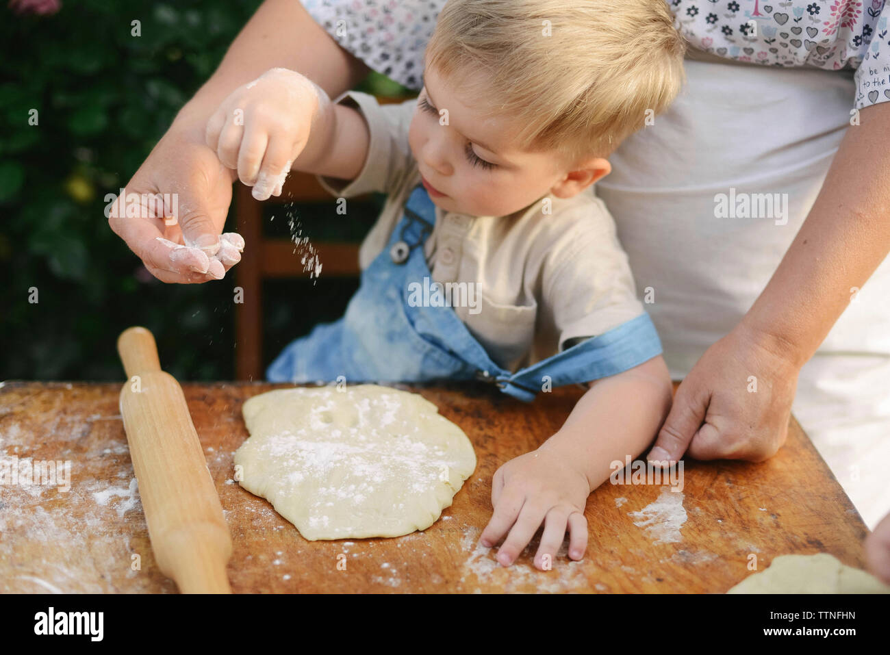 Midsection of mother with son preparing food on wooden table at yard Stock Photo
