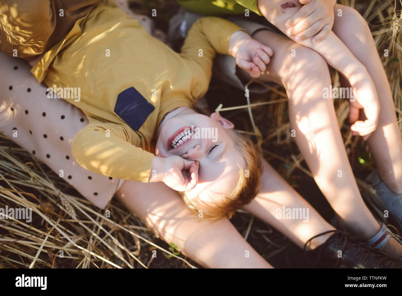 Boy rubbing eye while lying on mother's legs by brother on field Stock Photo
