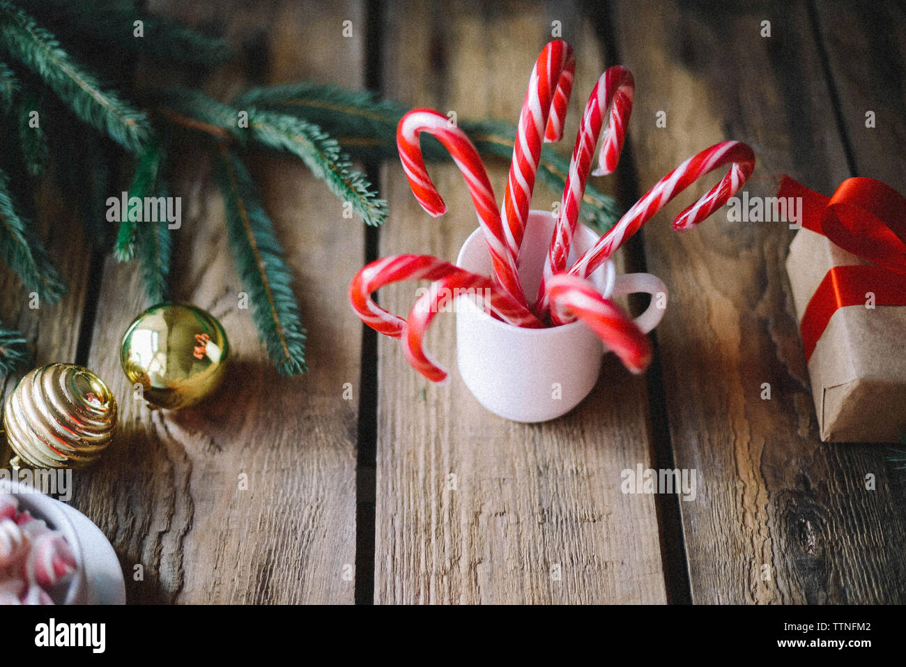 Close-up of candy canes in cup by baubles and twig on wooden table during christmas Stock Photo