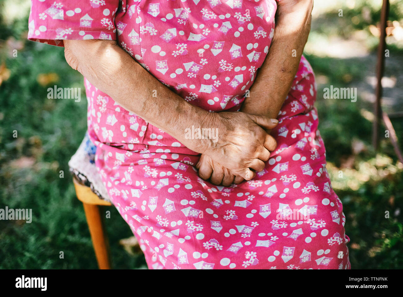 Midsection of senior woman with hands clasped sitting at backyard Stock Photo