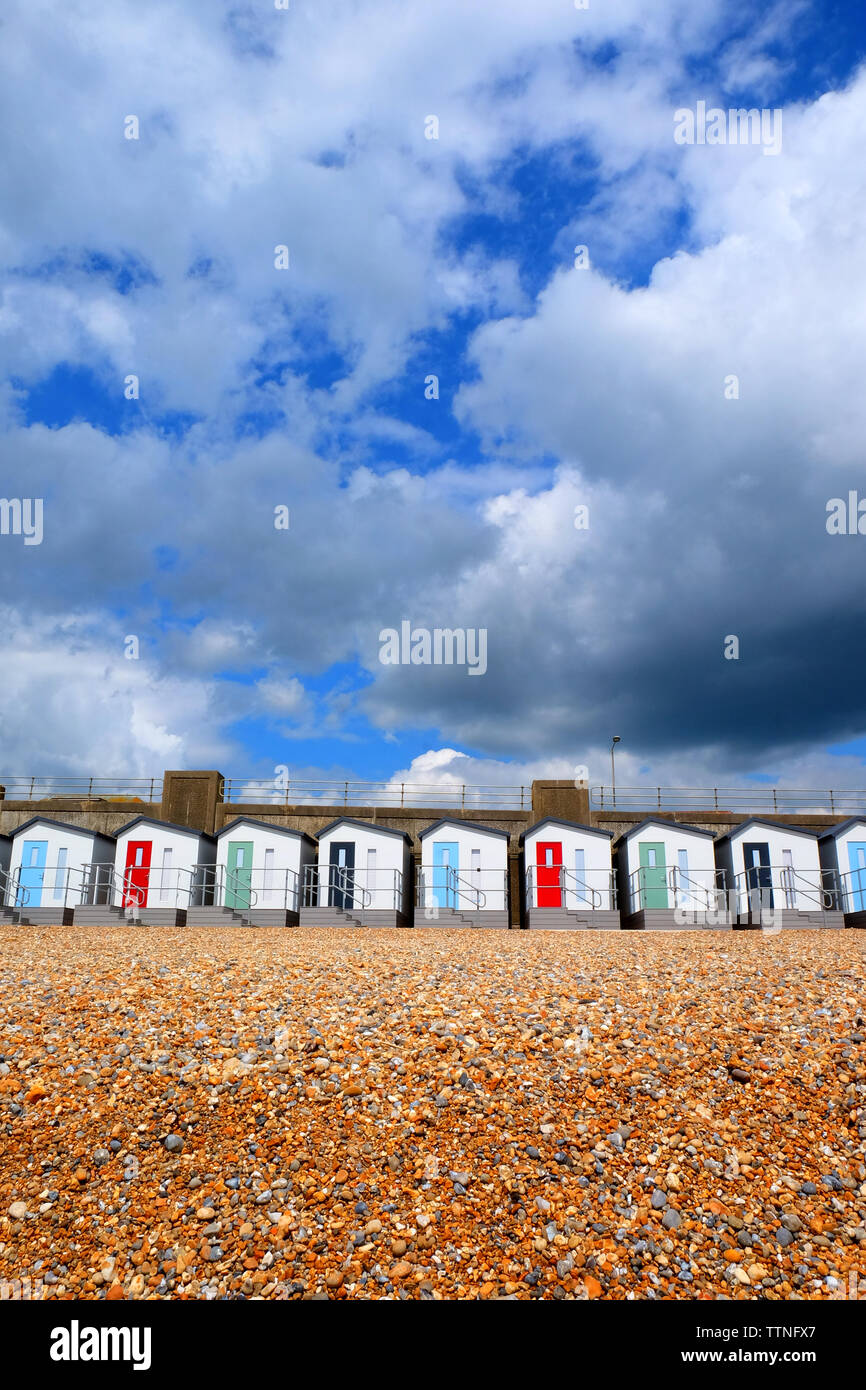 A line of 12 new Beach huts running through the centre of the image with red, blue and green doors and balconies, below is a yellow pebble beach and a Stock Photo