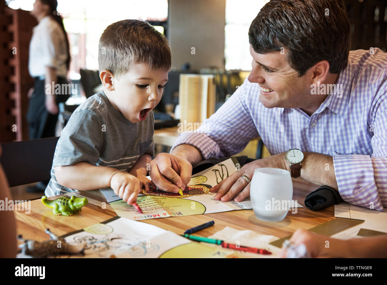 Happy father looking at shocked boy while coloring menu in restaurant Stock Photo