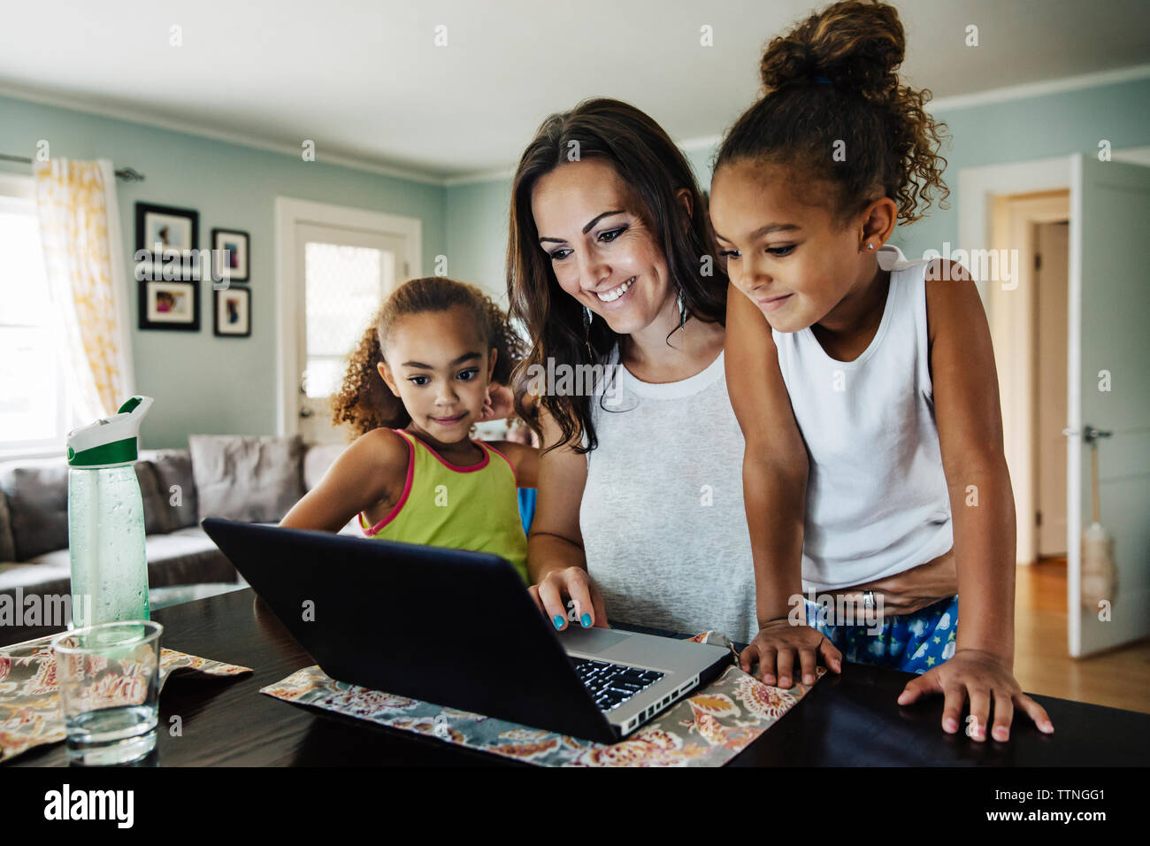 Happy woman using laptop with daughters at home Stock Photo