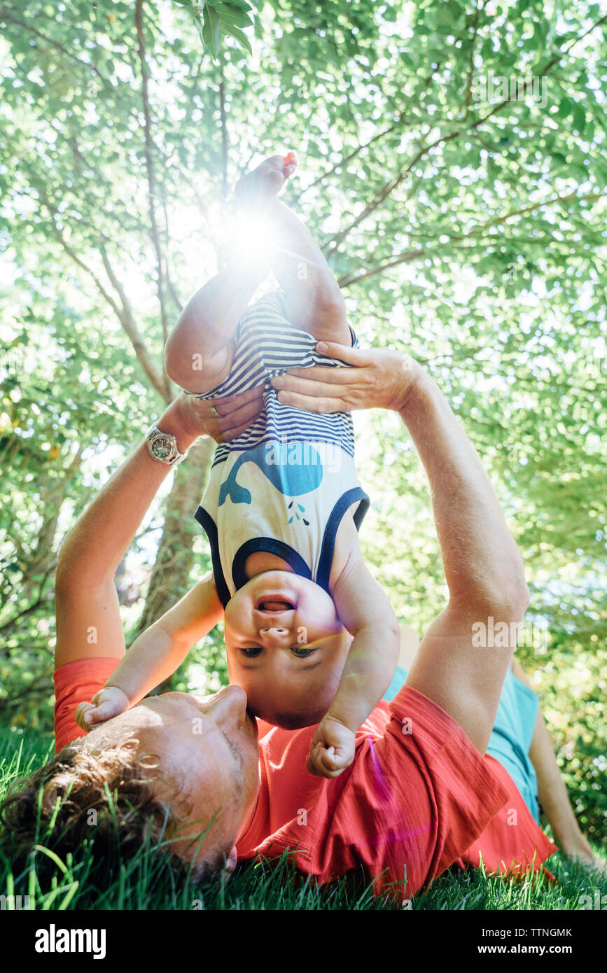Father holding baby upside down while lying in backyard Stock Photo