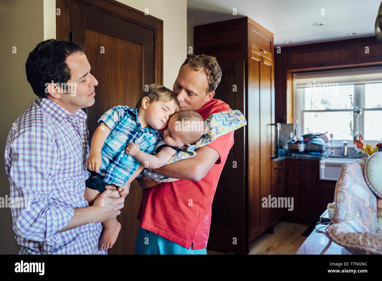 Homosexual couple holding sons at home Stock Photo