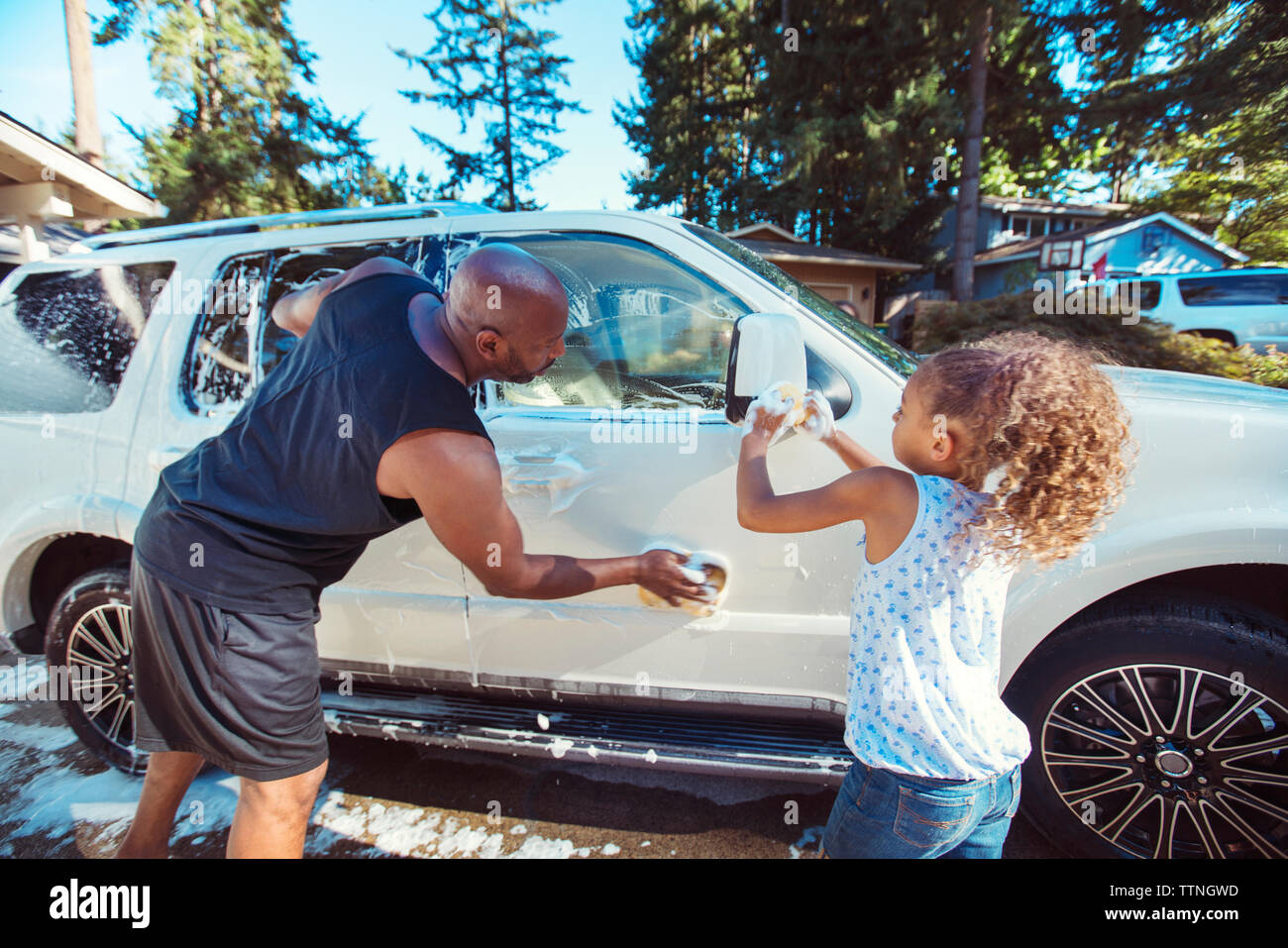 Father and daughter washing car in driveway Stock Photo
