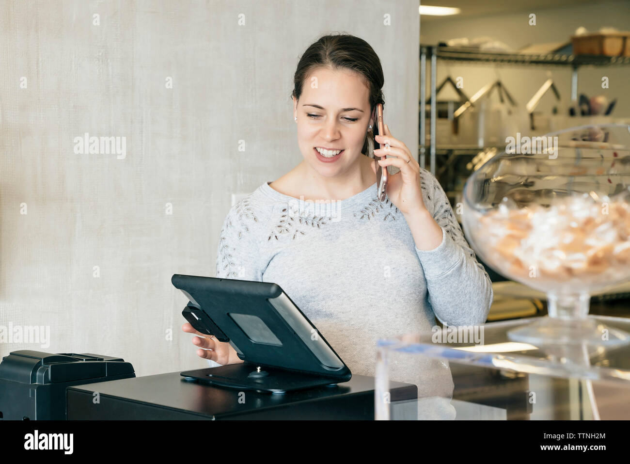 Woman talking on mobile phone while using tablet computer at store Stock Photo