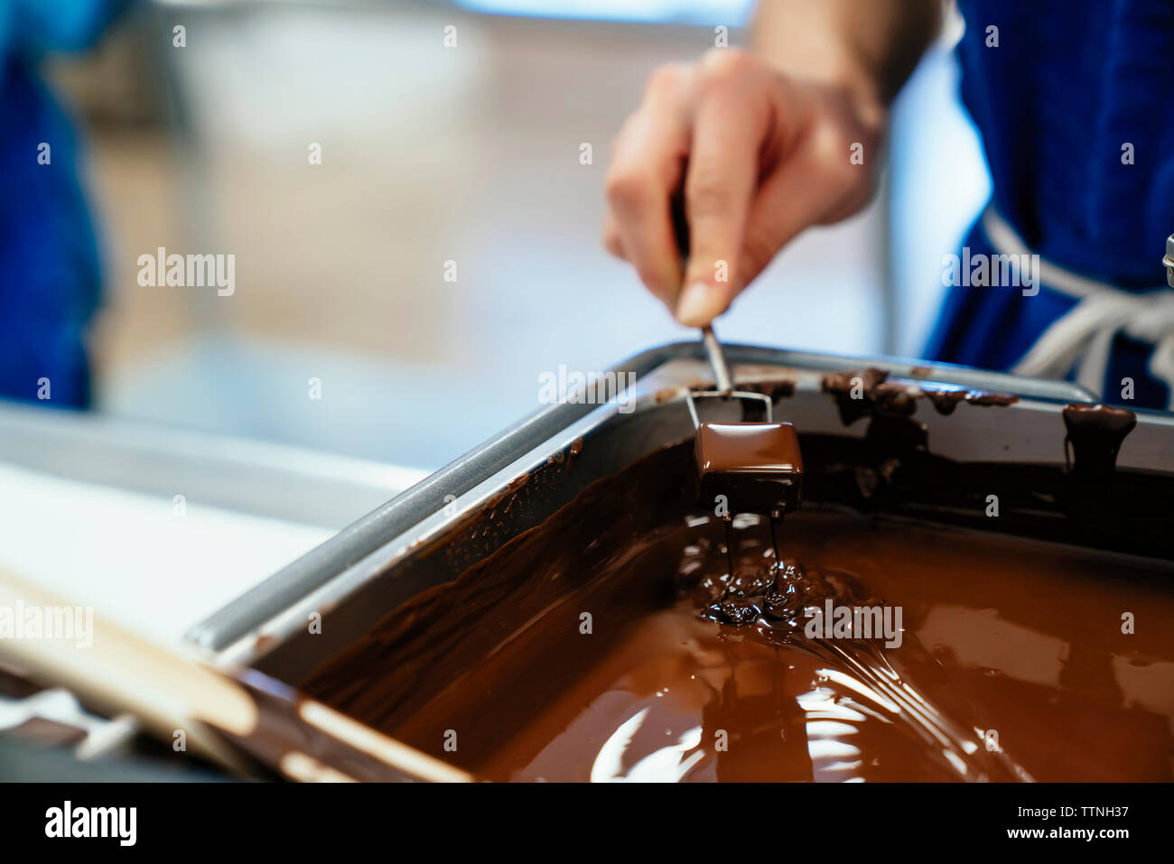 Cropped hand of female chef dipping chocolate in fondue at factory Stock Photo