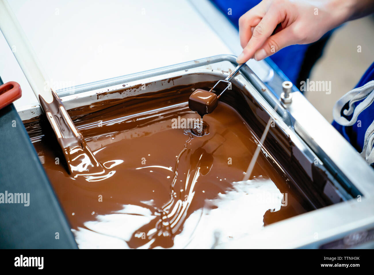 Cropped hand of female chef dipping chocolate with fork in fondue Stock Photo
