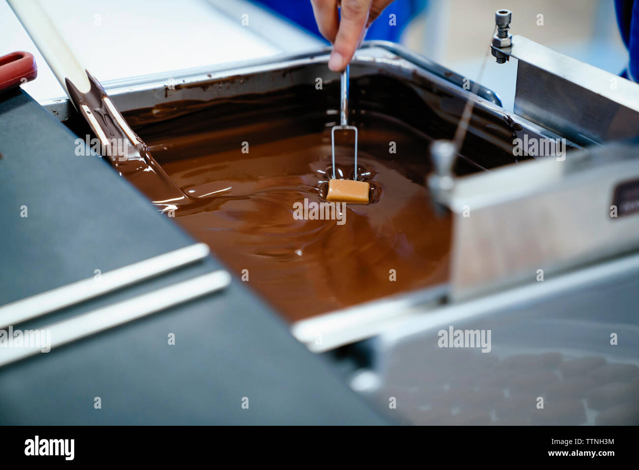 Cropped hand of female chef dipping chocolate with fork in fondue at factory Stock Photo