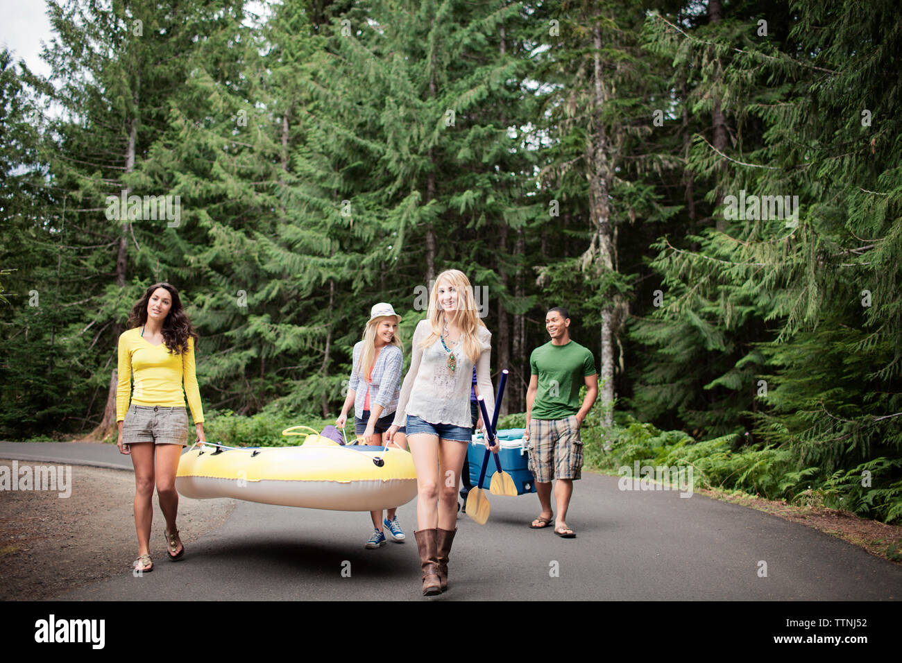 Friends carrying inflatable raft while walking on country road Stock ...