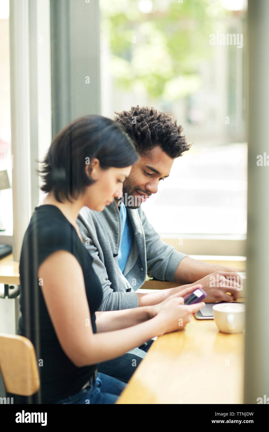 Multi-ethnic couple using smart phone in cafe Stock Photo