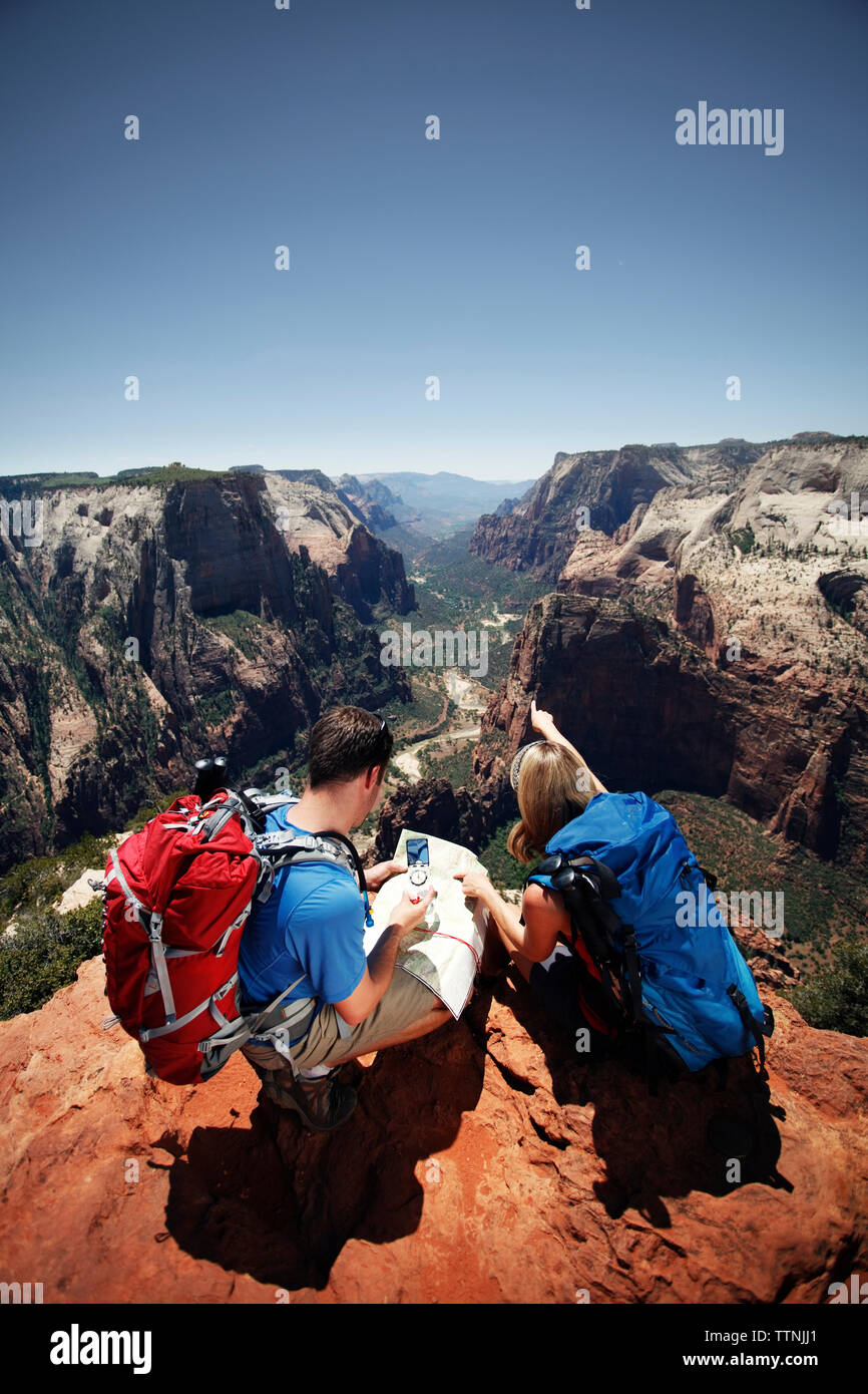 Hikers checking map while sitting at mountain cliff Stock Photo