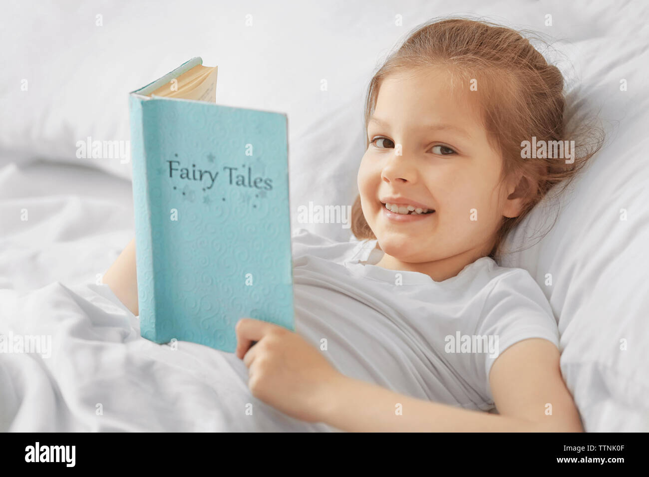 Cute girl with book in white bed Stock Photo Alamy