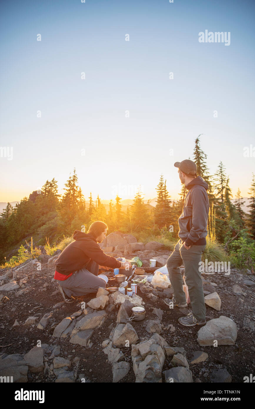 Hikers preparing food on mountain against clear sky during sunset Stock Photo